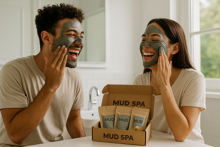 two young adults laughing in a bright bathroom while smearing rich gray mud masks on their faces